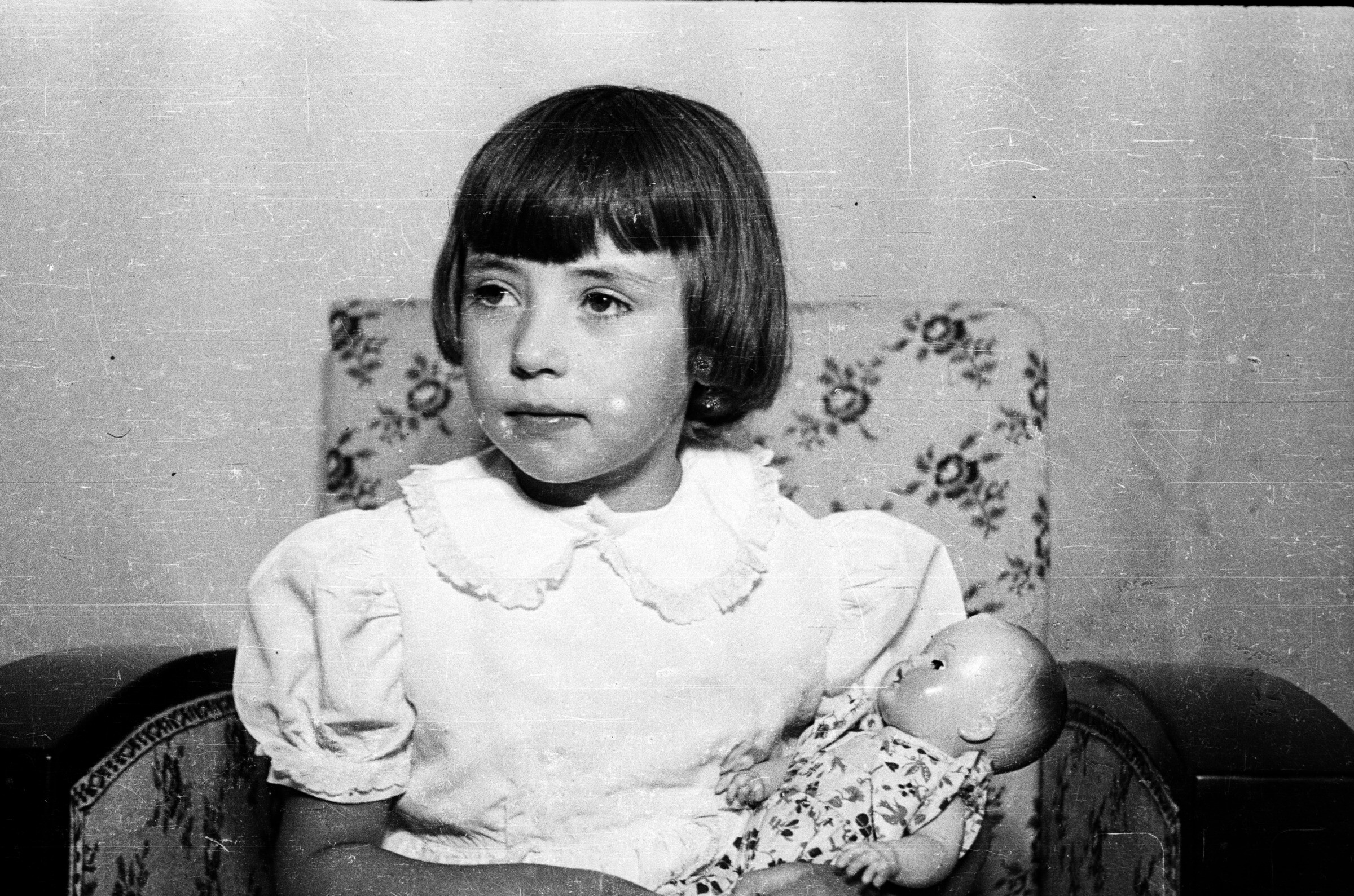 Retrato de plano medio de María Eugenia Carstens Delgado sentada en un sillón, posando junto a su muñeca