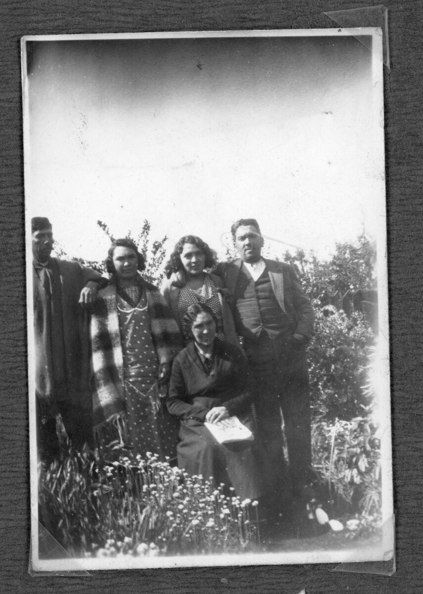 Retrato grupal de dos hombres adultos y tres mujeres adultas en entorno rural, rodeados de flores y vegetación.