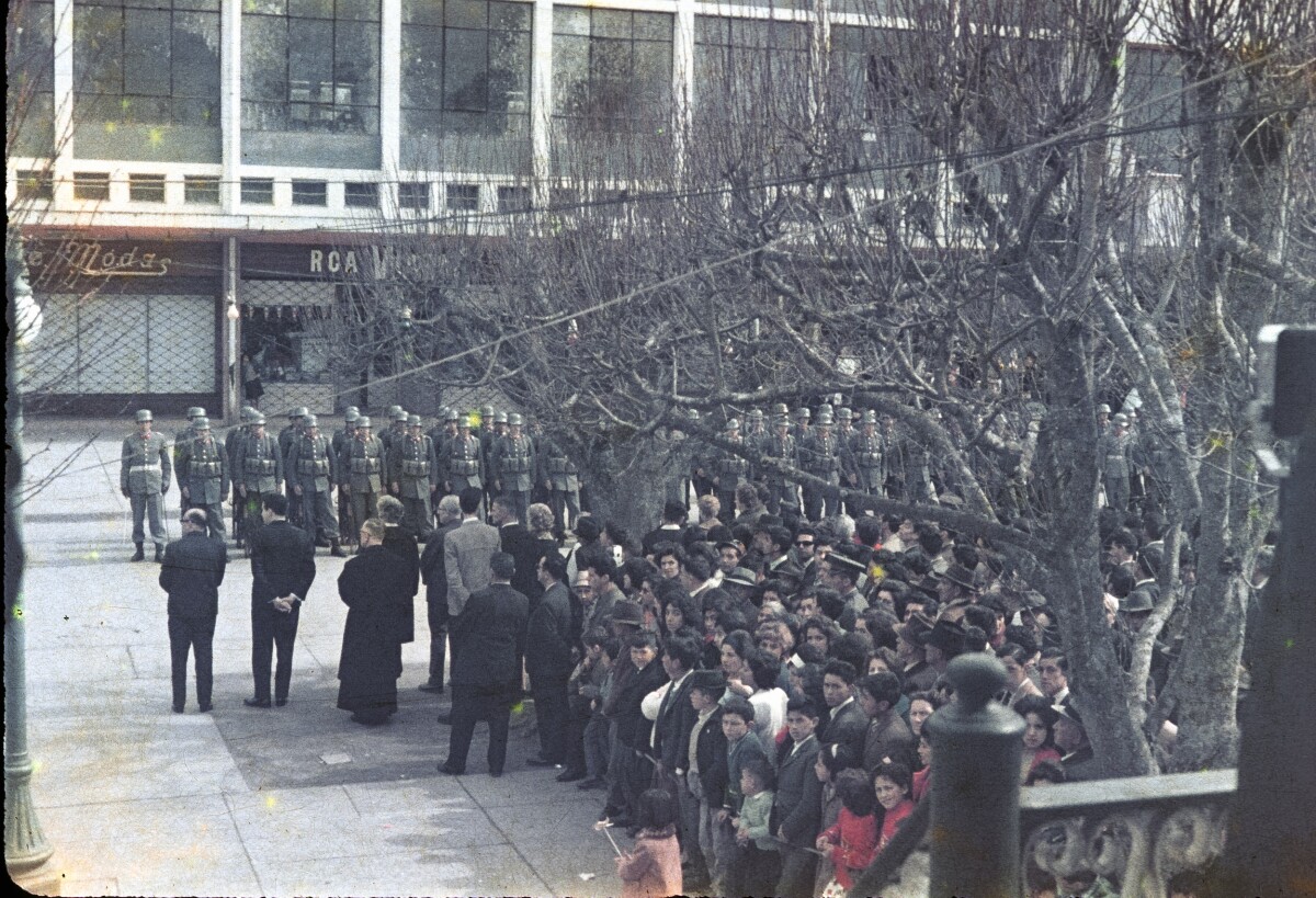 Plano entero de militares desfilando mientras un grupo de personas y autoridades los miran desde la otra vereda. Imagen capturada desde el templete de Plaza de la Concordia