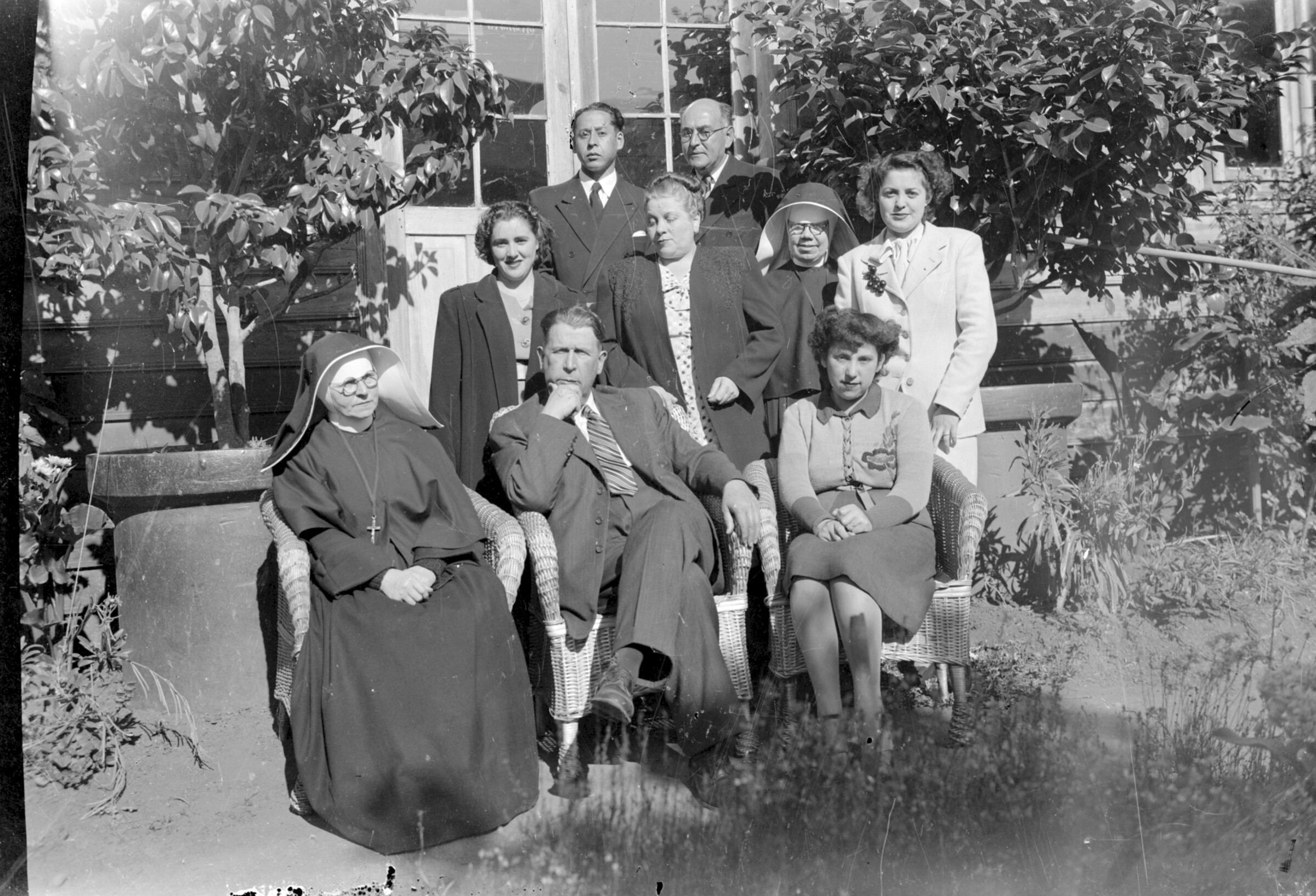 Plano general de un grupo de hombres y mujeres y dos monjas posando en el patio de una casa
