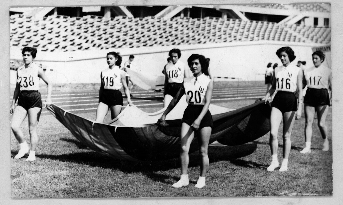 -plano general de un grupo de atletas, desfilando mientras sostienen el borde de una bandera de gran tamaño. en sus poleras llevan distintos números y las siglas --LU-- por La Unión, durante un zonal sur de atletismo realizado en Tomé-
